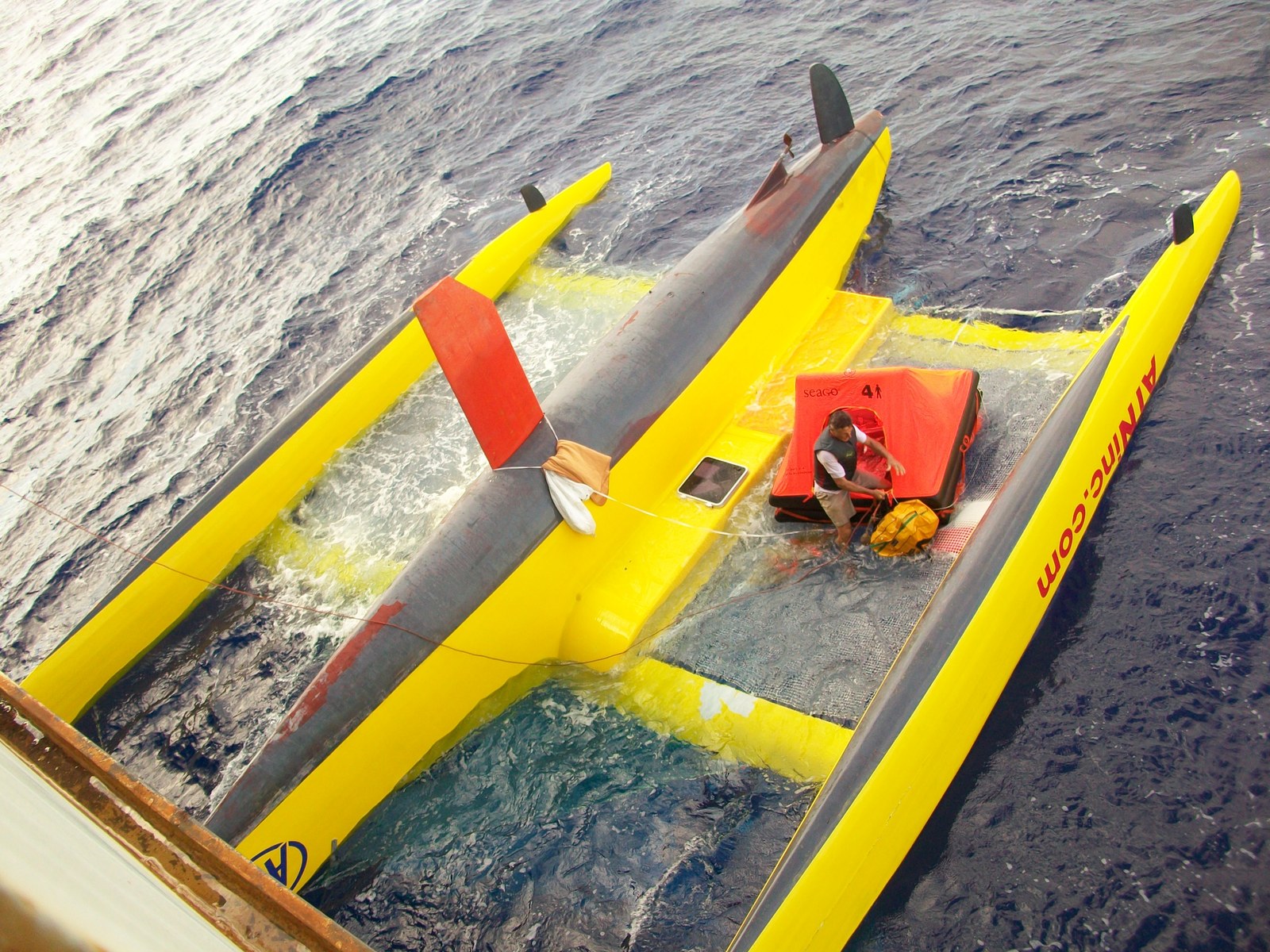 Etienne Giroire standing on the hull of his capsized trimaran with his liferaft, photographed from the rescue ship during the 2010 Route du Rhum