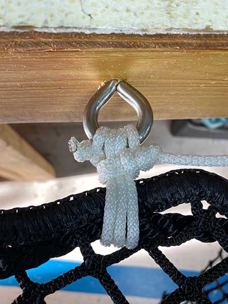 A finished lashing tied through a stainless pad eye, securing a black net to a timber beam